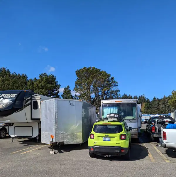 Backing up an RV into a tight space. Trailer next to it with green jeep in front.