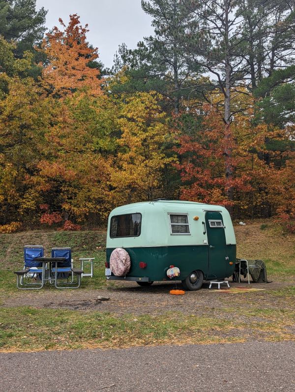 There were monthly rates at RV parks on this stay. Pictured is a small green camper with fall colors around it. 