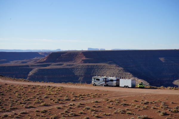 Campers with generators like our Class A motorhome next to a canyon with red dirt in the foreground let you camp anywhere. There is a silver trailer and a lime green jeep behind the motorhome. 