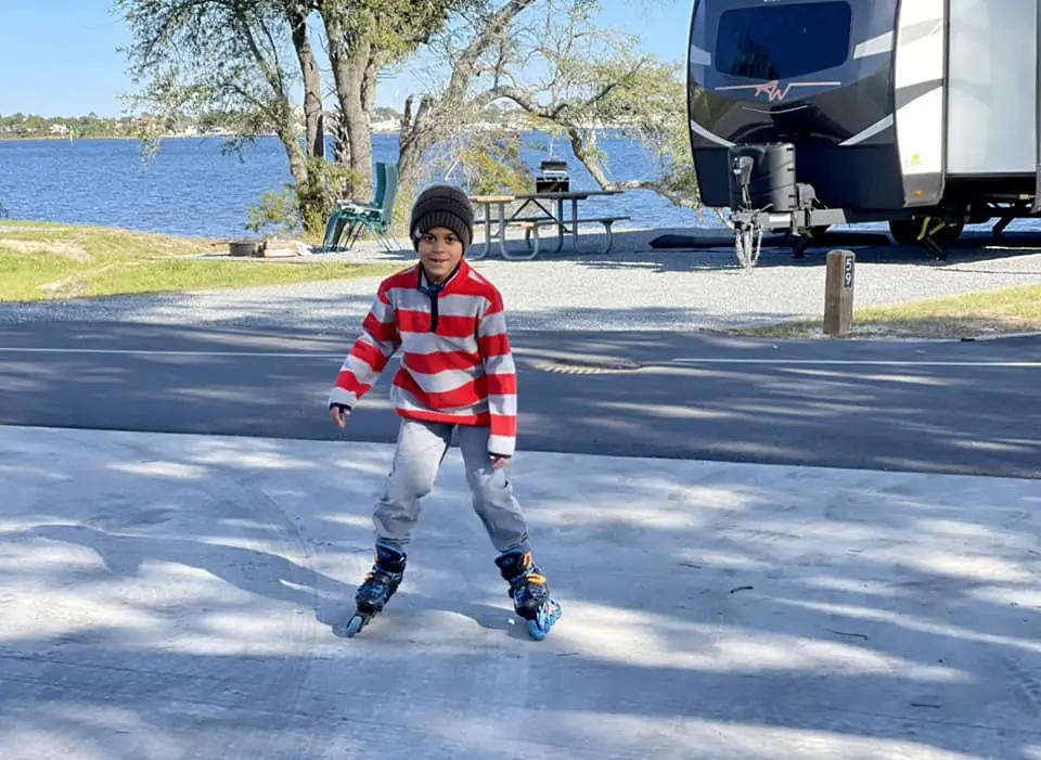 Pictured is Amber's son rollerblading and smilling near their RV which is parked right next to the water