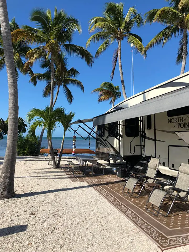 Palm trees surround an RV with its awning out and reclining chairs set out. The RV is right on the sand at this Florida RV beach resort and the ocean is just steps away. 