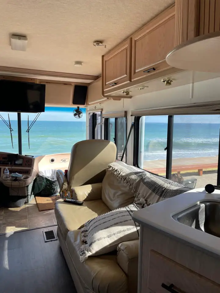 Photo from inside an RV looking out the window to the sand and ocean just outside the door 