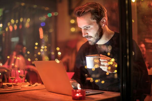 If RV internet options aren't available you may have to visit a coffee shop or other place to access the internet like this man holding a coffee cup and looking at his laptop.